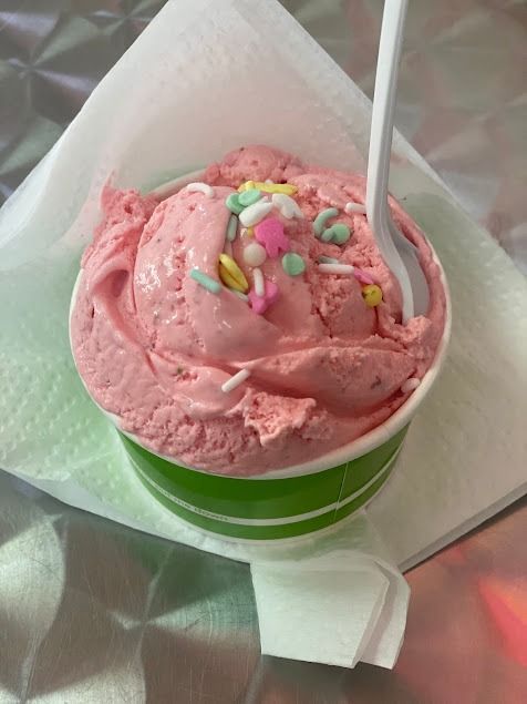 Pink ice cream in a green cup with colorful sprinkles, wrapped in a white napkin.
