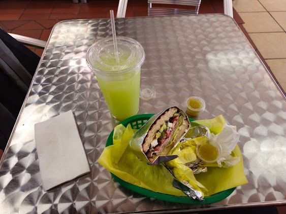 Green drink and sandwich on a metal table with lime wedges and napkins in a casual café.