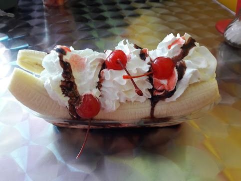 Banana split sundae with whipped cream, cherries, and chocolate drizzle in a glass dish