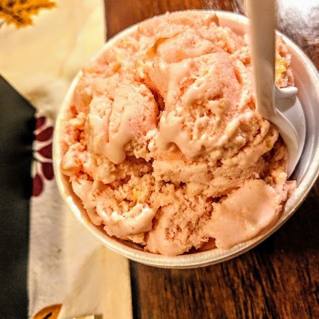 Scoops of pink ice cream in a cup on a wooden table with a spoon