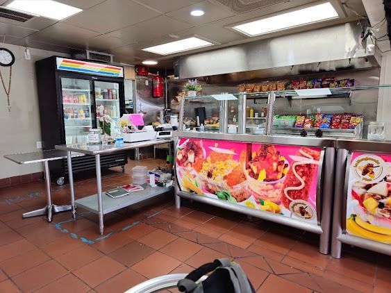 Small deli counter with stainless tables, glass display cases, and colorful food posters in a tiled shop interior