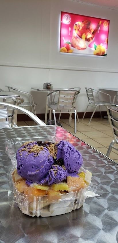 Purple-frosted cupcake in a clear plastic container on a metal table inside a bright café