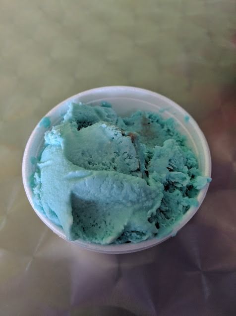 Mint-green ice cream in a white cup on a patterned table.