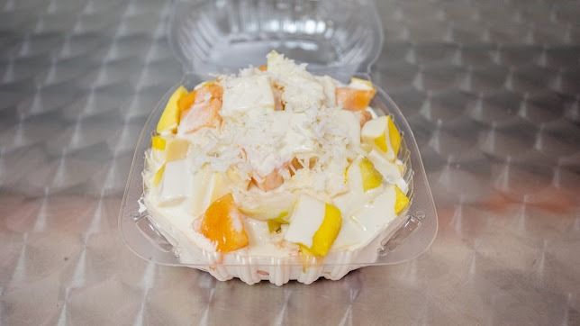 Dessert cup topped with whipped cream, shredded coconut, and yellow-orange fruit pieces