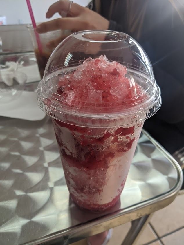 Red shaved-ice drink in a clear plastic cup with lid and straw on a tray