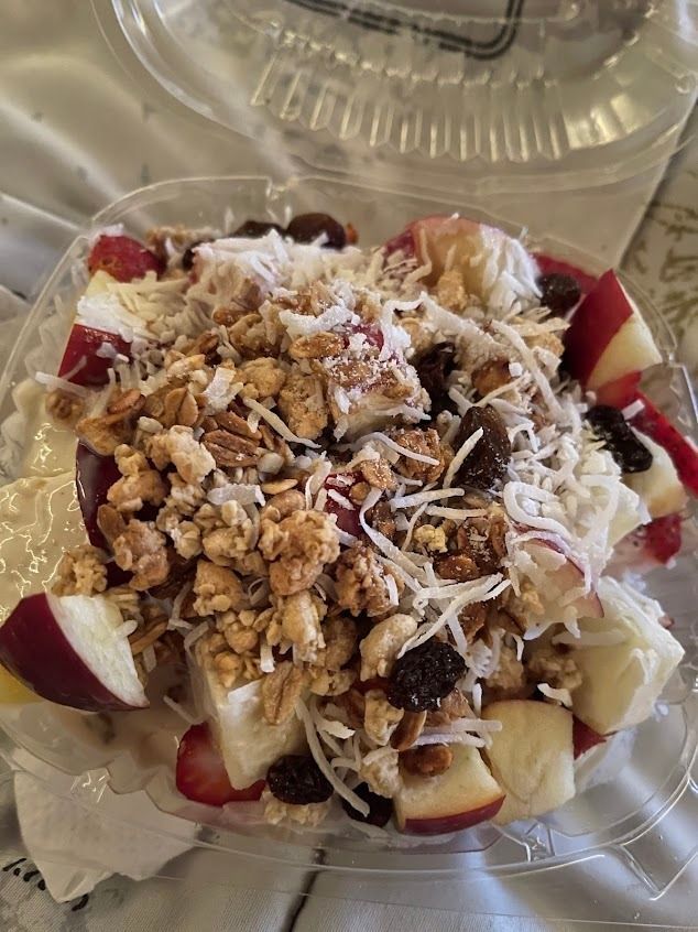Dessert cup with granola, shredded coconut, and strawberry-topped fruit pieces in a clear plastic container