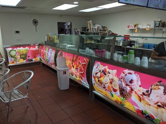 Ice cream shop interior with pink menu panels, glass display case, and metal chairs on tiled floor