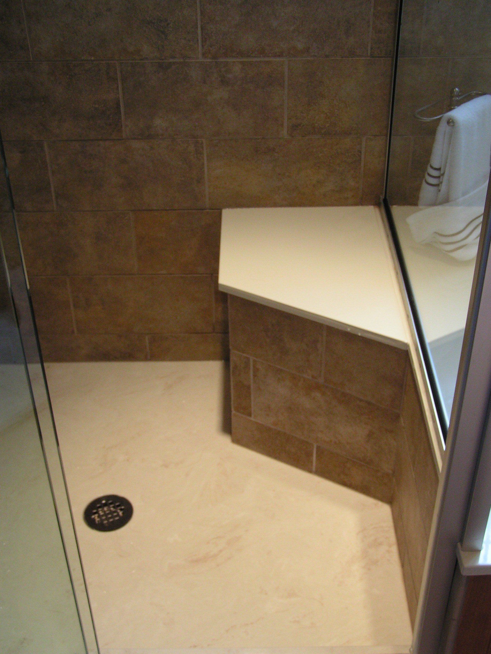 Shower stall with brown tiled walls, beige floor, and a white bench.
