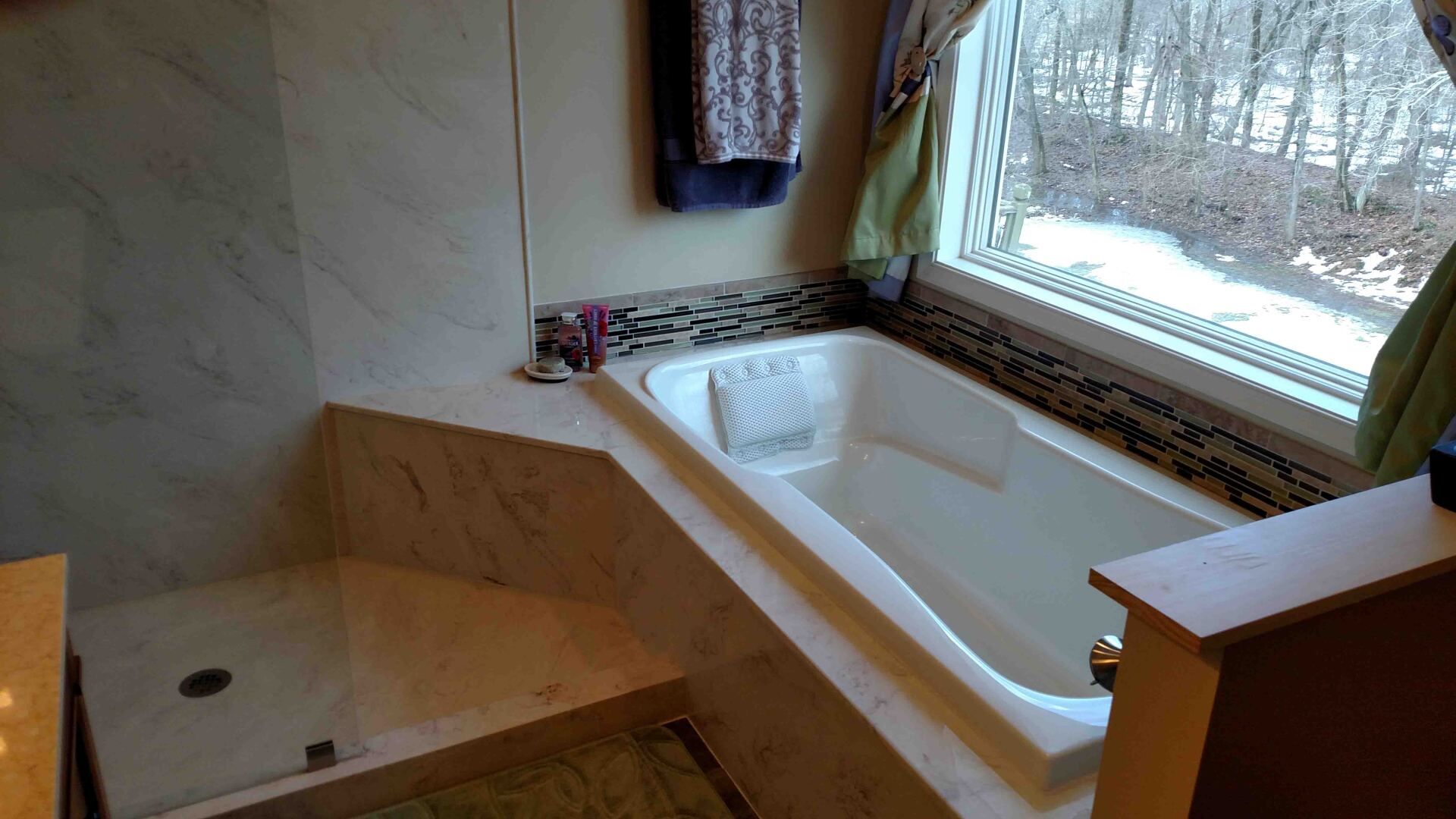 Bathroom with a built-in white bathtub, marble tile, and a window with a view.