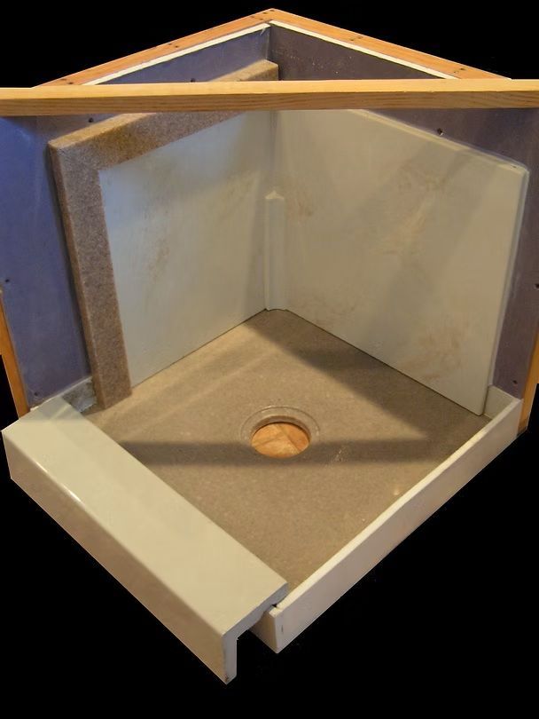 A cross-section view of a neutral-colored shower pan and wall surround system set within a wooden frame.