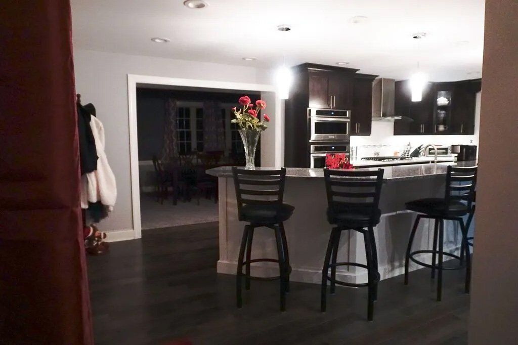 Interior view of a kitchen with a gray island, bar stools, and dark cabinets. A bouquet of roses sits on the island.