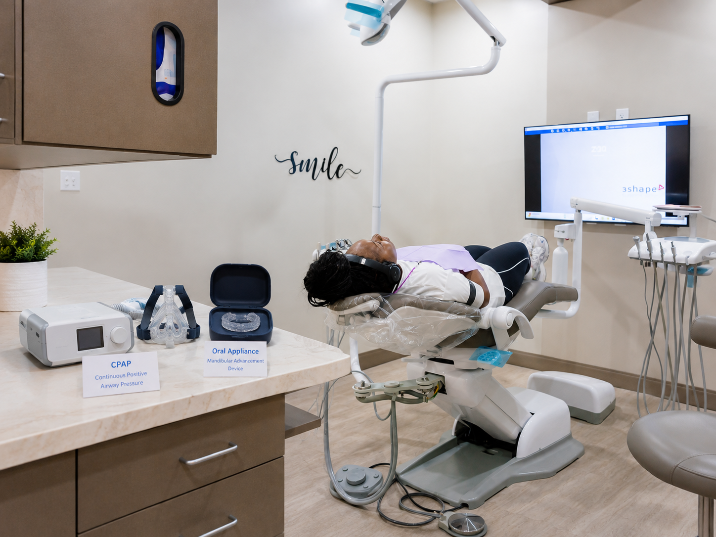 Dental clinic with patient reclined in chair, dentist working beside monitor and instruments on counter.