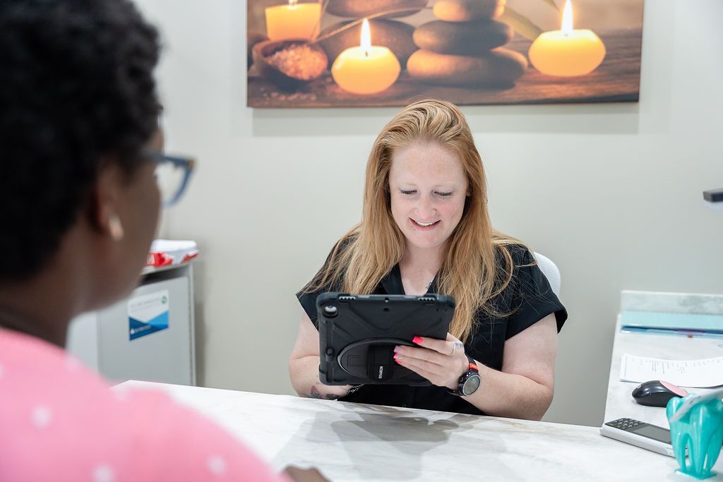 Woman at a desk smiling at a tablet in a bright office reception area.