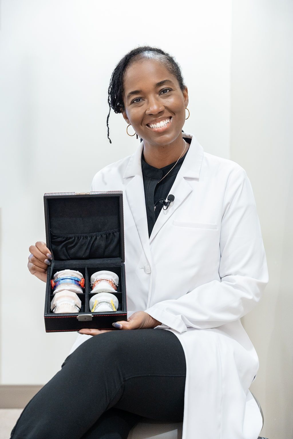 Smiling lab professional in a white coat holding an open black case with two supplement bottles.