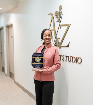 Woman holding a plaque and smiling in a studio hallway beside a wall logo.