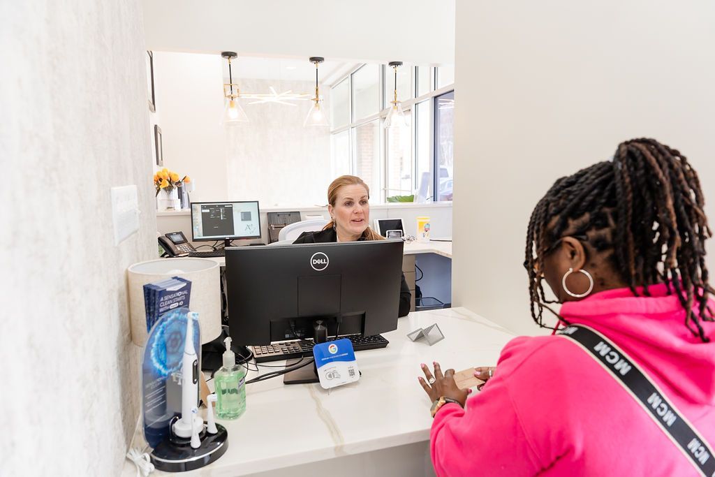 Person at bank counter speaking with teller across computer monitor