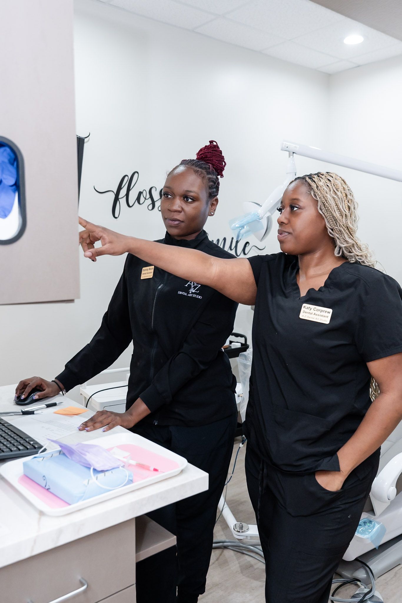 Two women in black scrubs point toward a wall display in a bright office reception area.