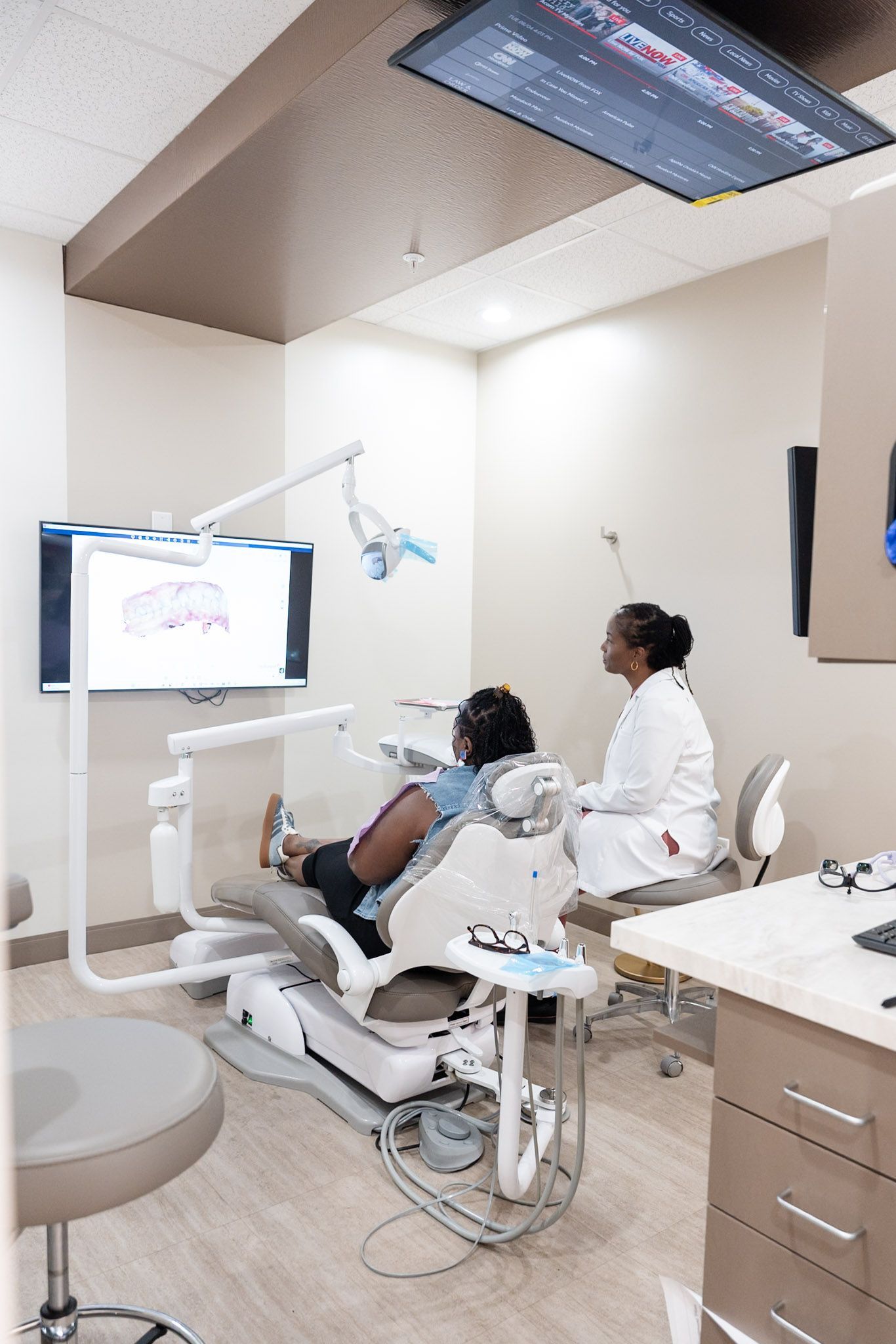 Dentist treating a patient in a modern clinic with a chair, monitor, and ceiling-mounted TV