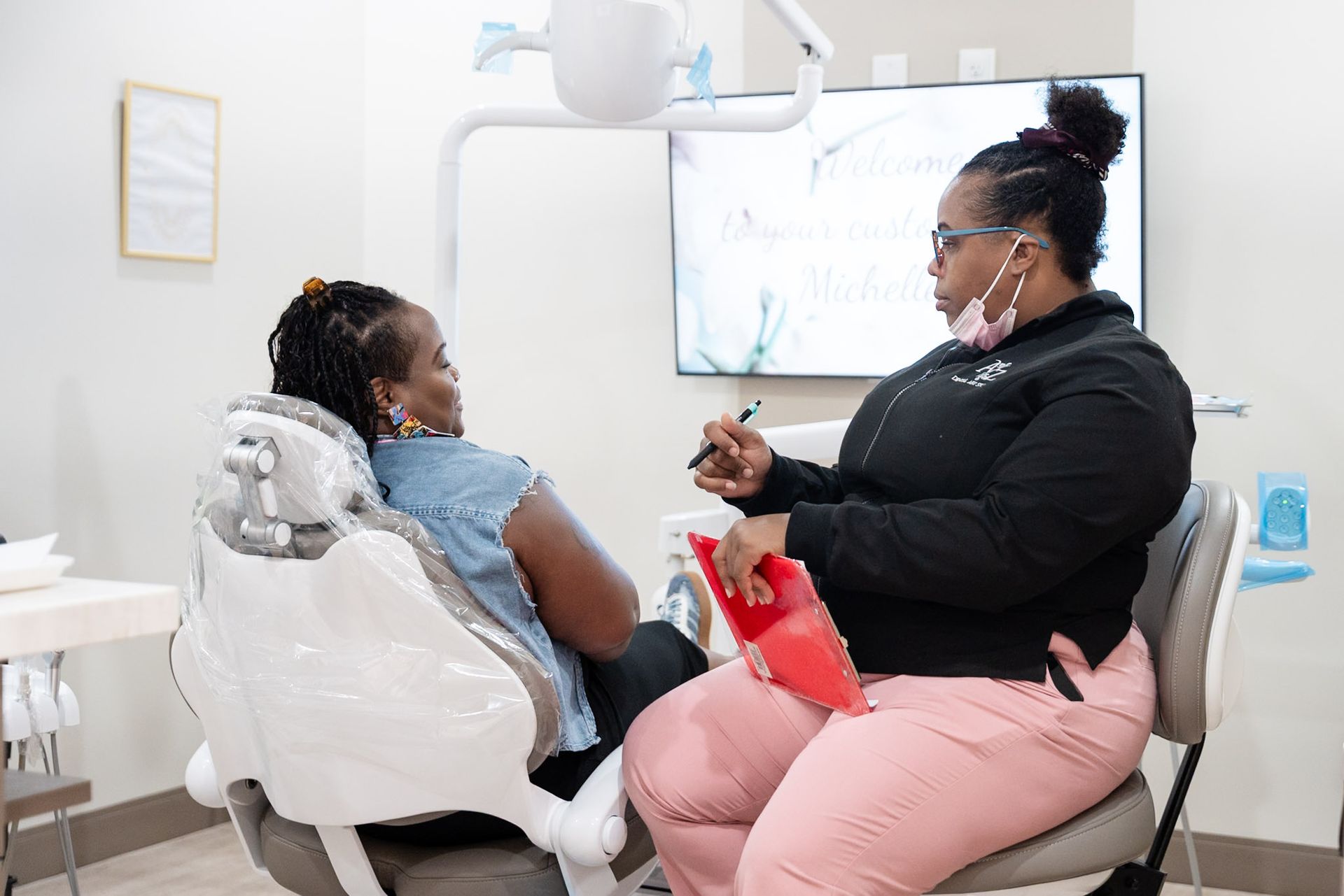Dental patient and dentist talking in a bright clinic, with a red bib and dental equipment nearby