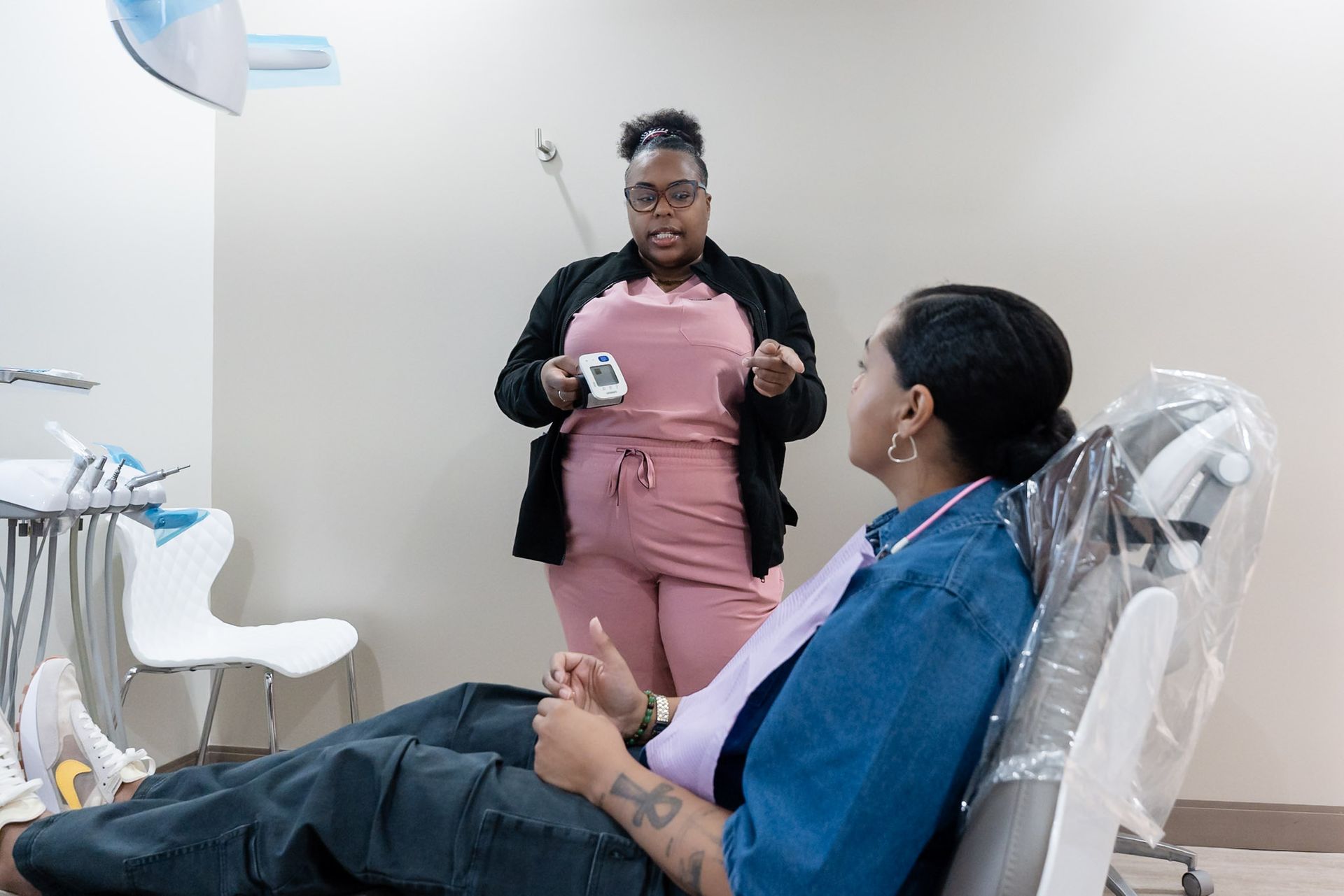 Dental hygienist speaking with seated patient in a clinic, holding a cup in a modern dental chair area