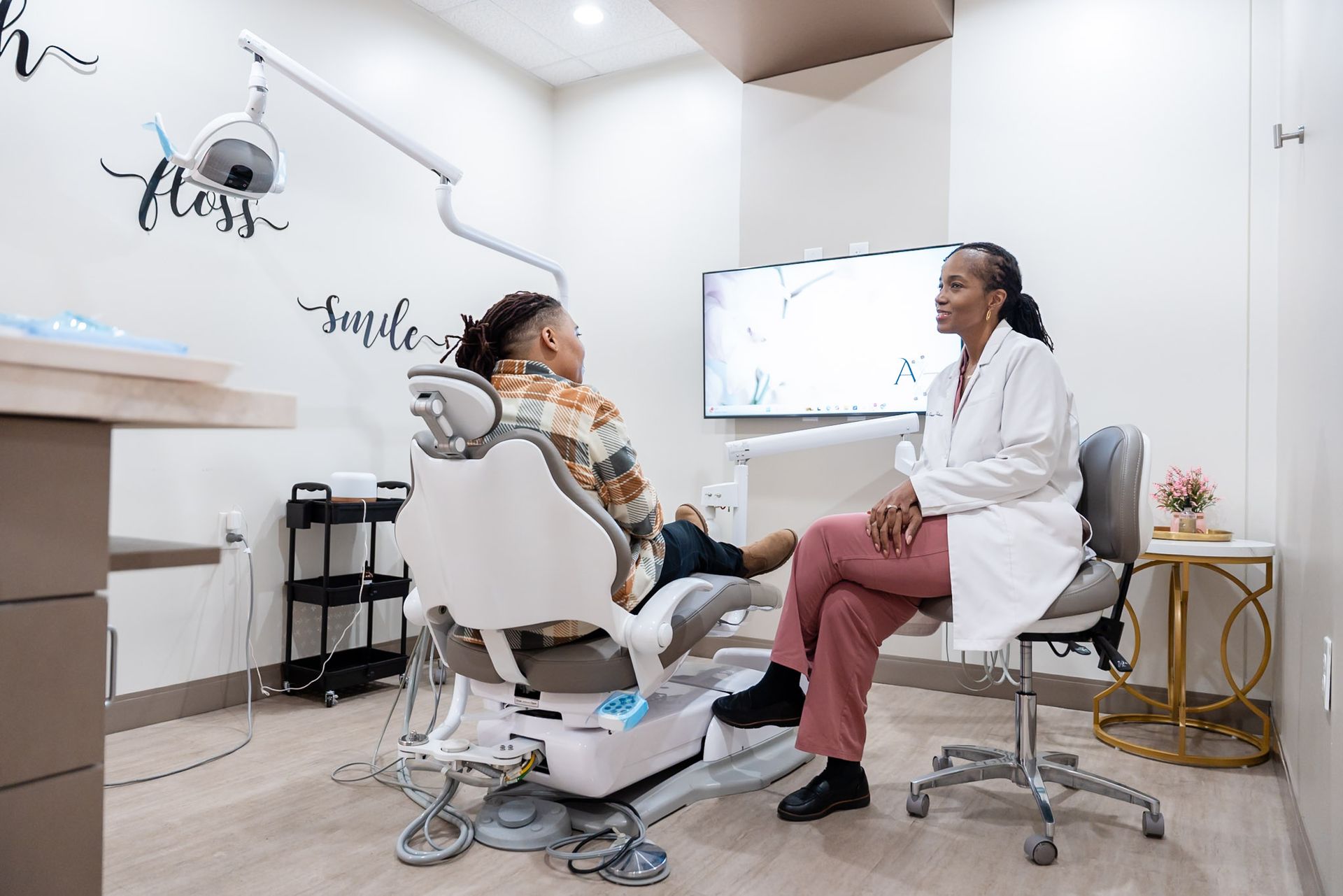 Doctor consulting with a seated patient in a bright exam room with a monitor and medical equipment.