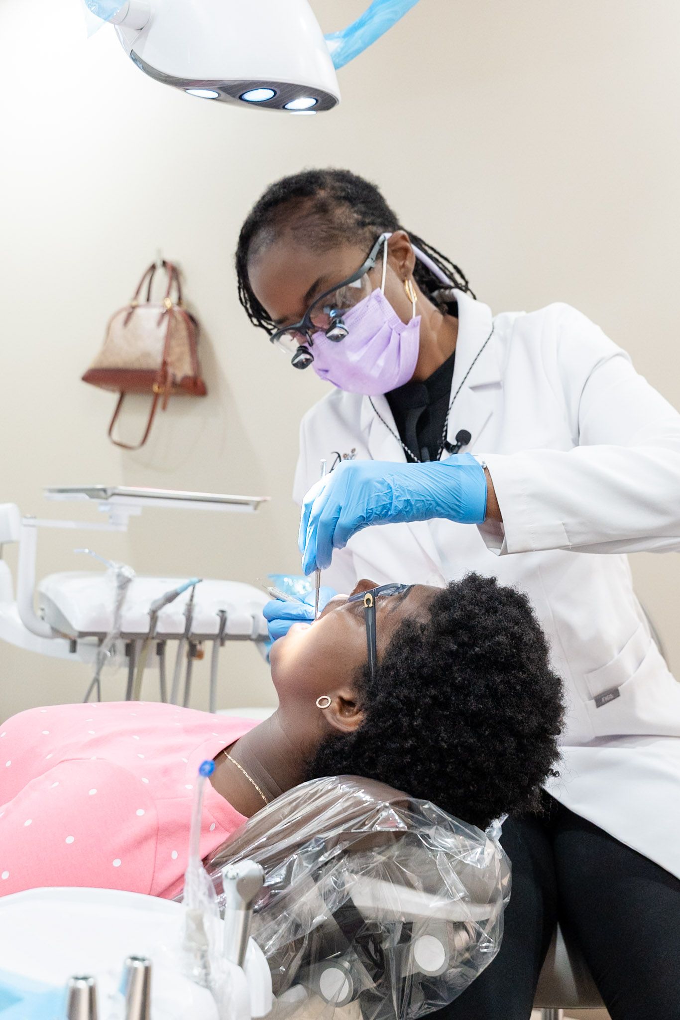 Dentist examining a patient in a dental chair, wearing gloves and a mask.