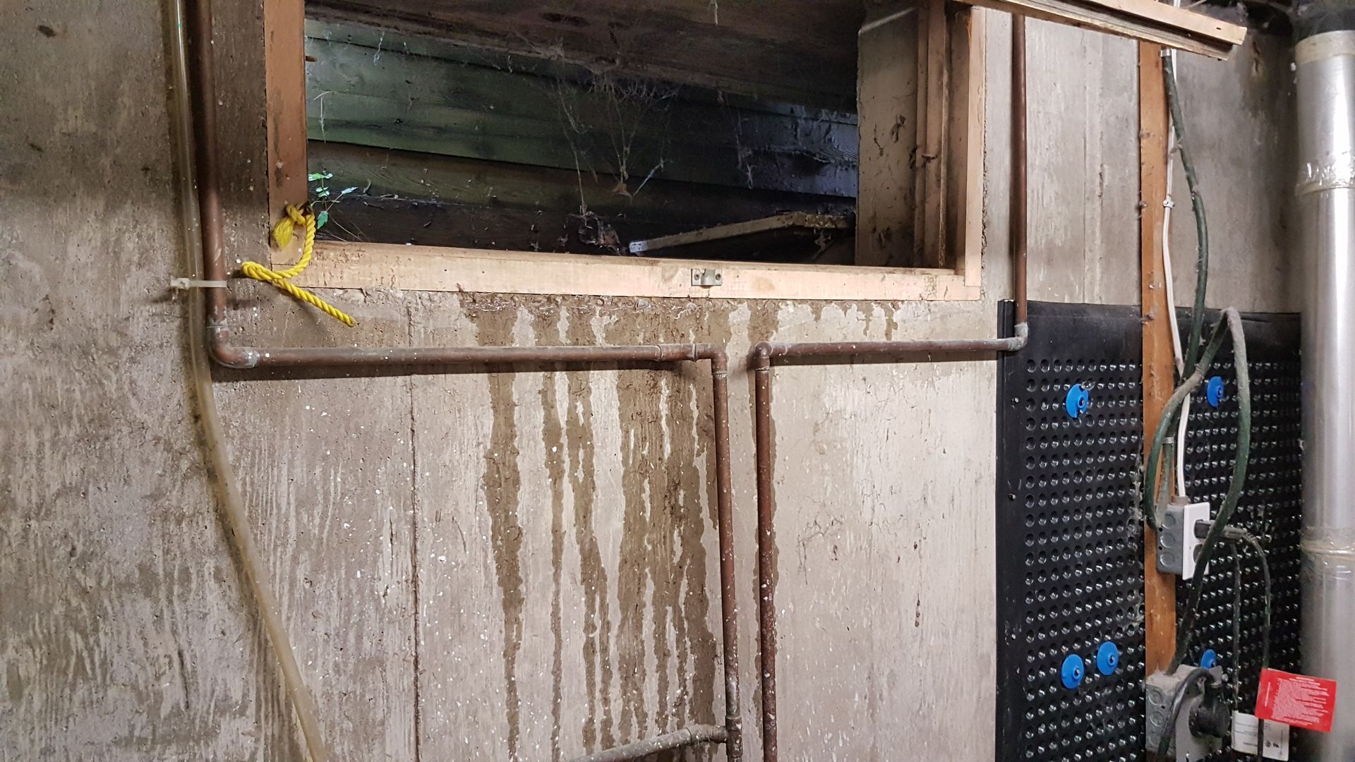 A concrete wall with a window and pipes coming out of it.