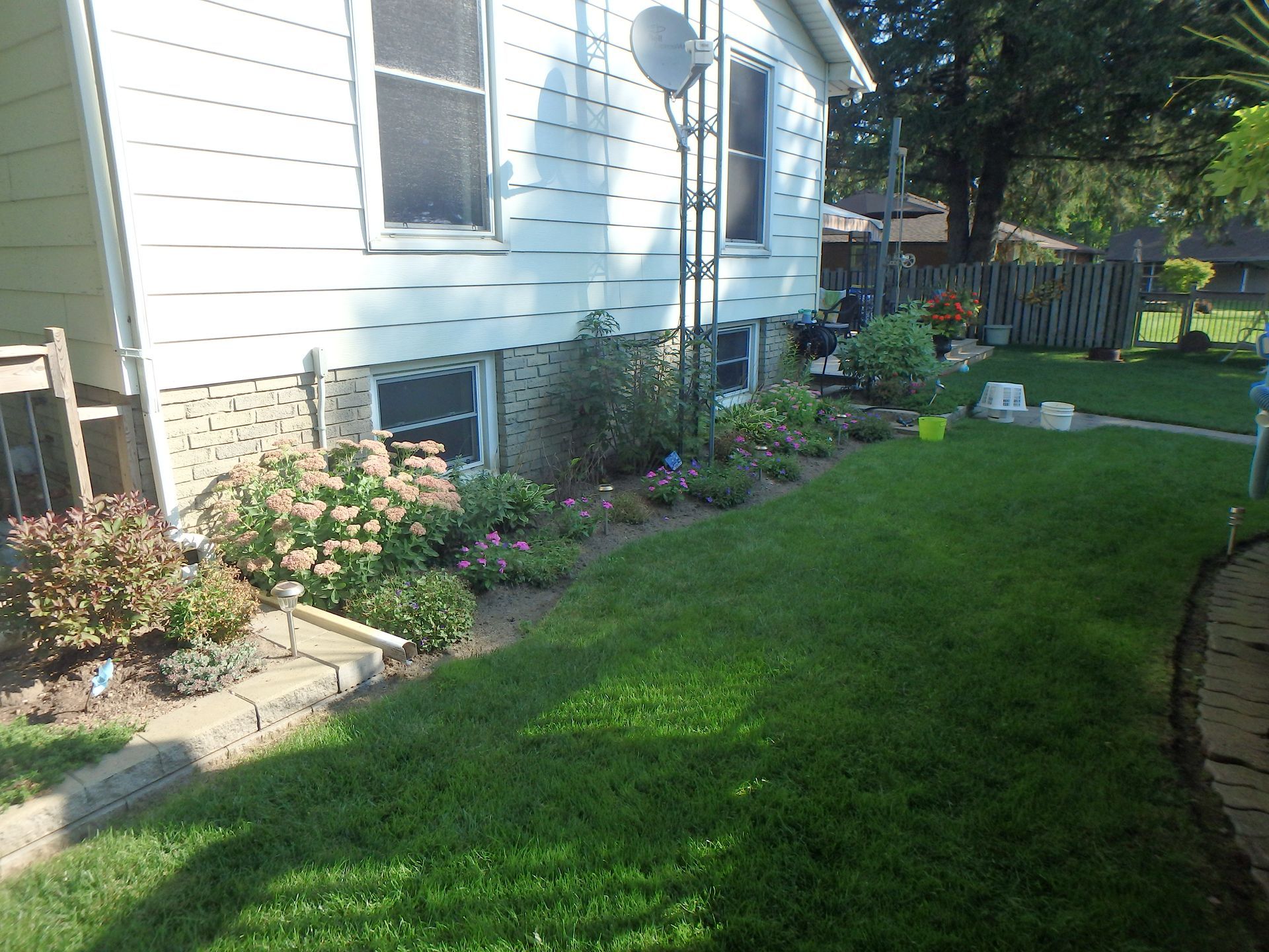Side view of a house with a well-maintained flower bed along its foundation and lush green lawn.