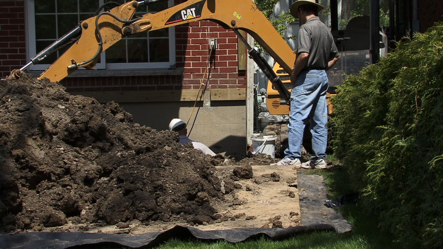 A man is standing next to a pile of dirt in front of a cat excavator.