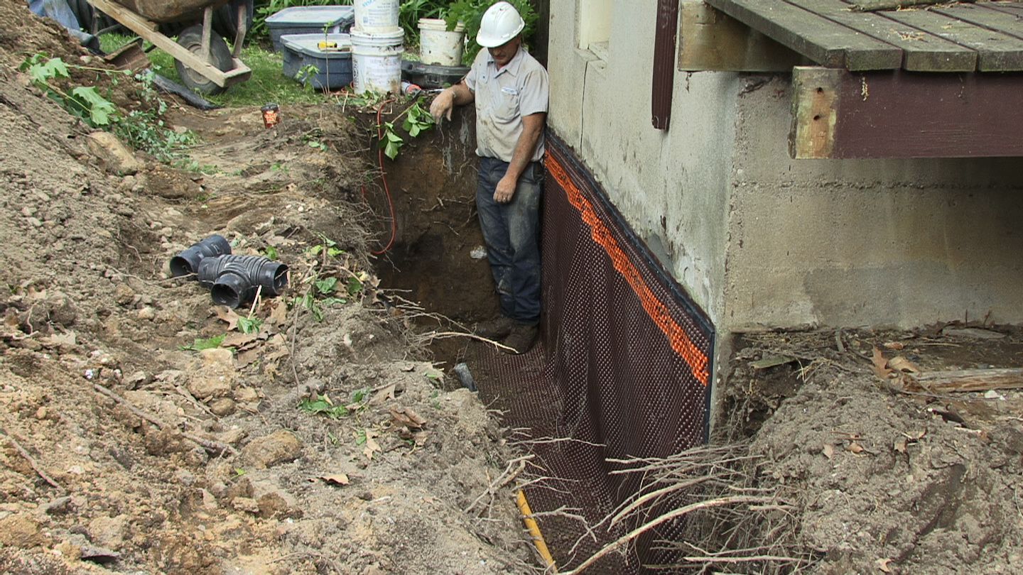 A man is digging a hole in the ground next to a house.