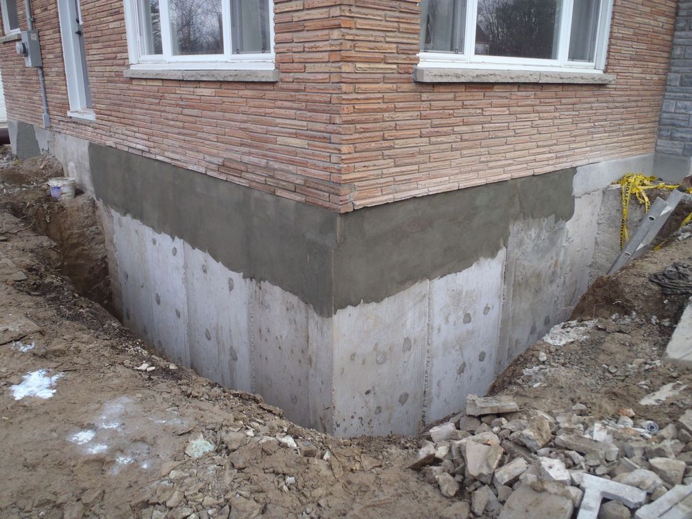 Brick house foundation under construction with exposed concrete basement walls and surrounding dirt trench