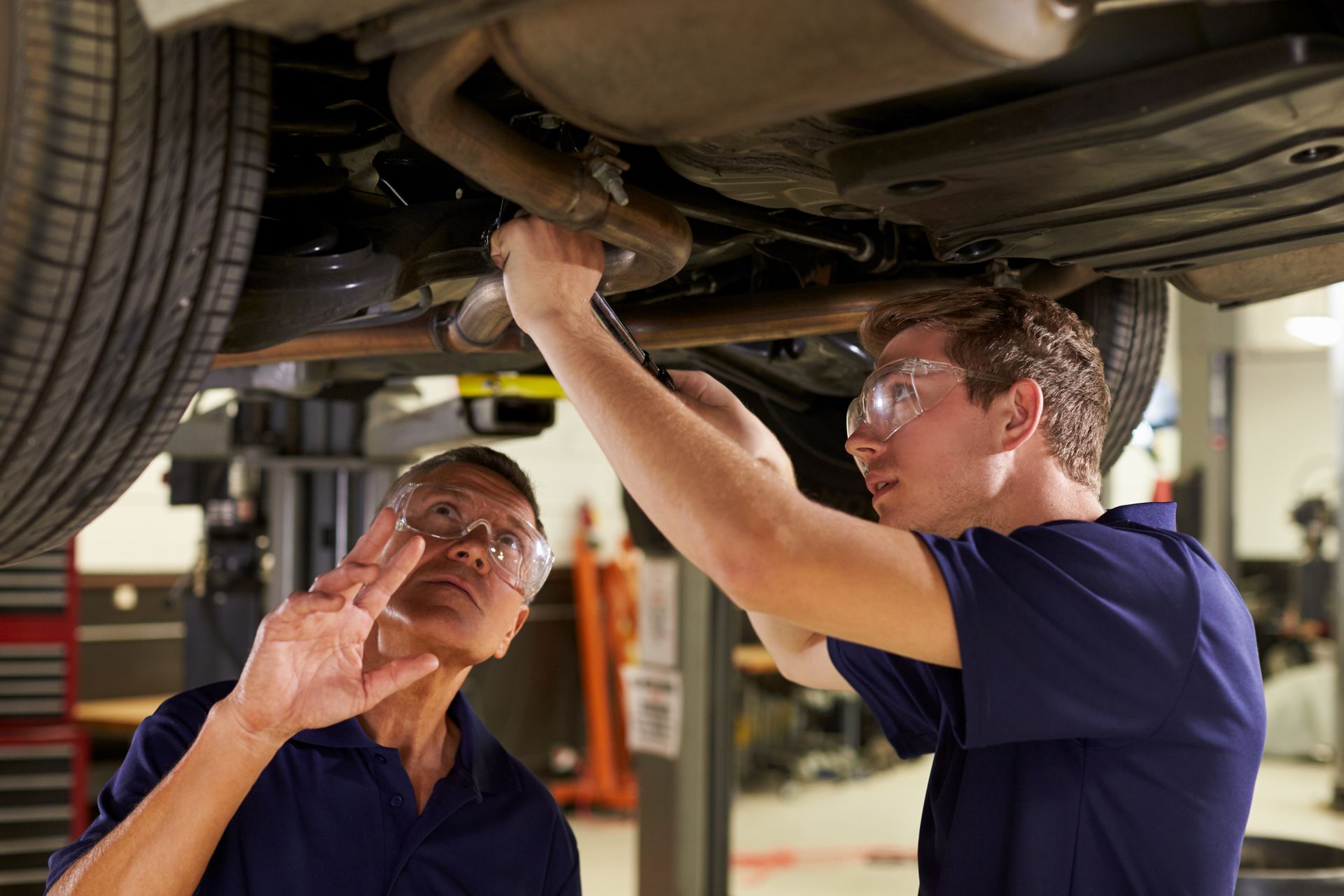 A technician wearing black gloves mounts a car tire onto a silver rim using a blue tire changer machine in a shop.