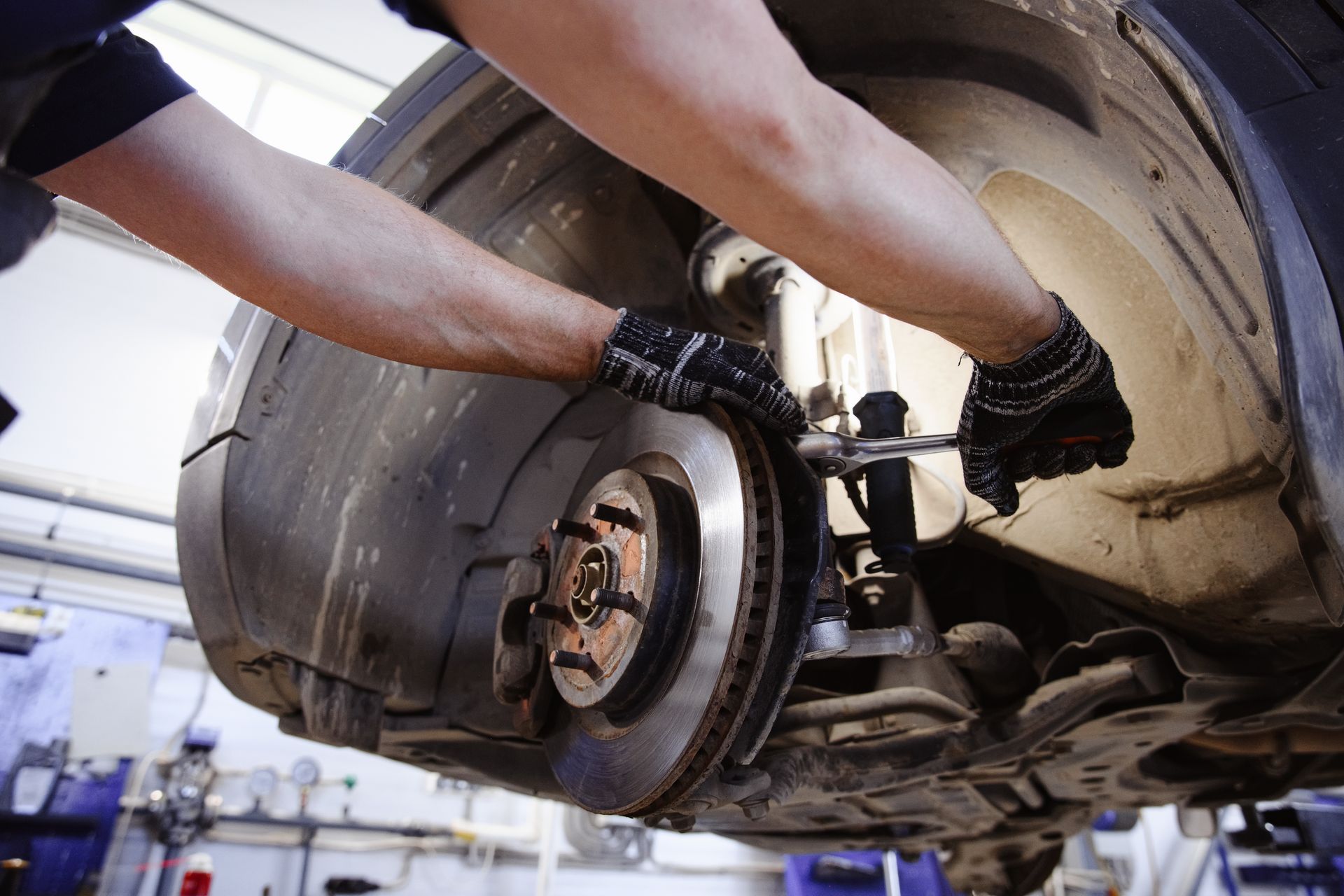 Mechanic working on a car's brake system with a wrench in a garage.