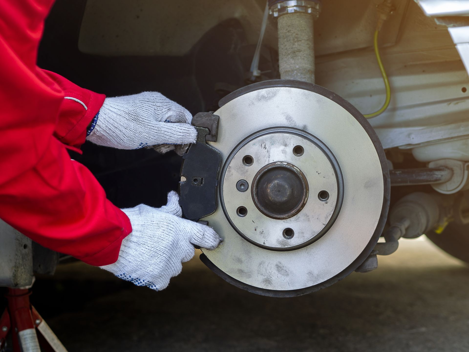 A technician wearing black gloves mounts a car tire onto a silver rim using a blue tire changer machine in a shop.