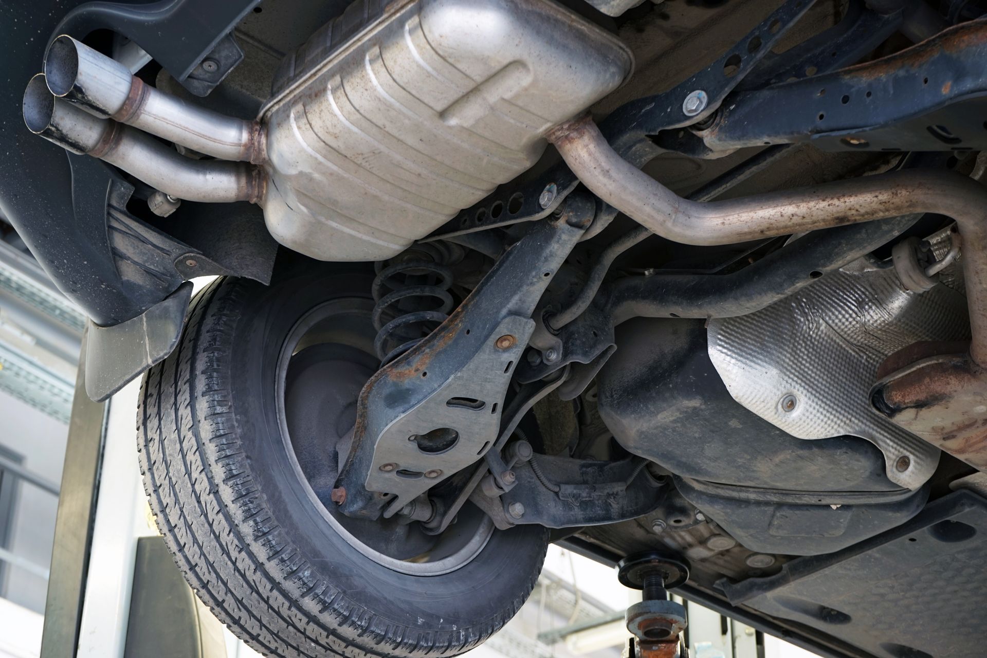 Underside of a car on a lift; exhaust system, tire, suspension visible.