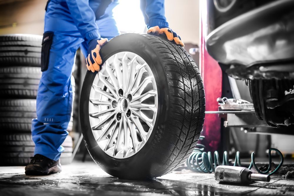 A mechanic wearing a blue uniform uses a tire balancing machine to service a vehicle wheel in an auto repair shop.