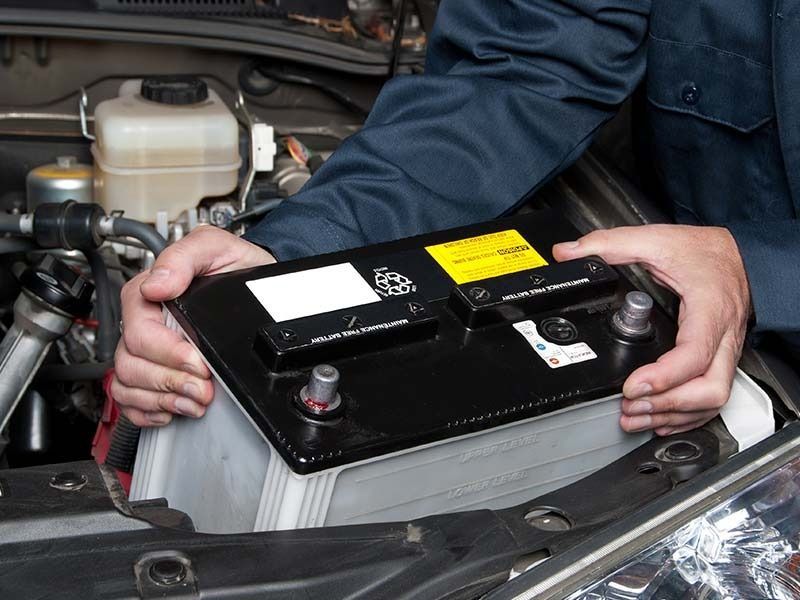 Person placing a new car battery into an engine compartment.