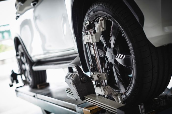 White car tire being aligned on a lift. Grey machinery attaches to the tire's rim.