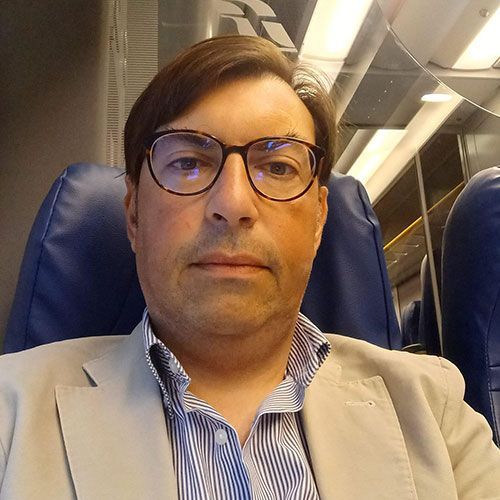 Un uomo che indossa occhiali e un abito è seduto su una sedia blu.