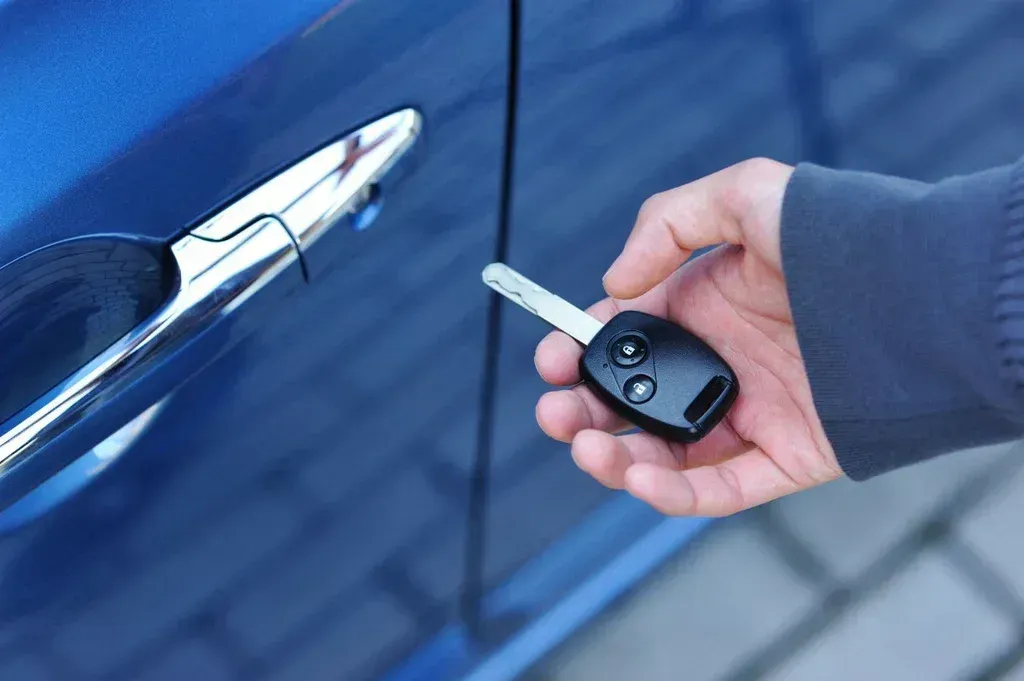 Hand holding car key next to a blue car door.