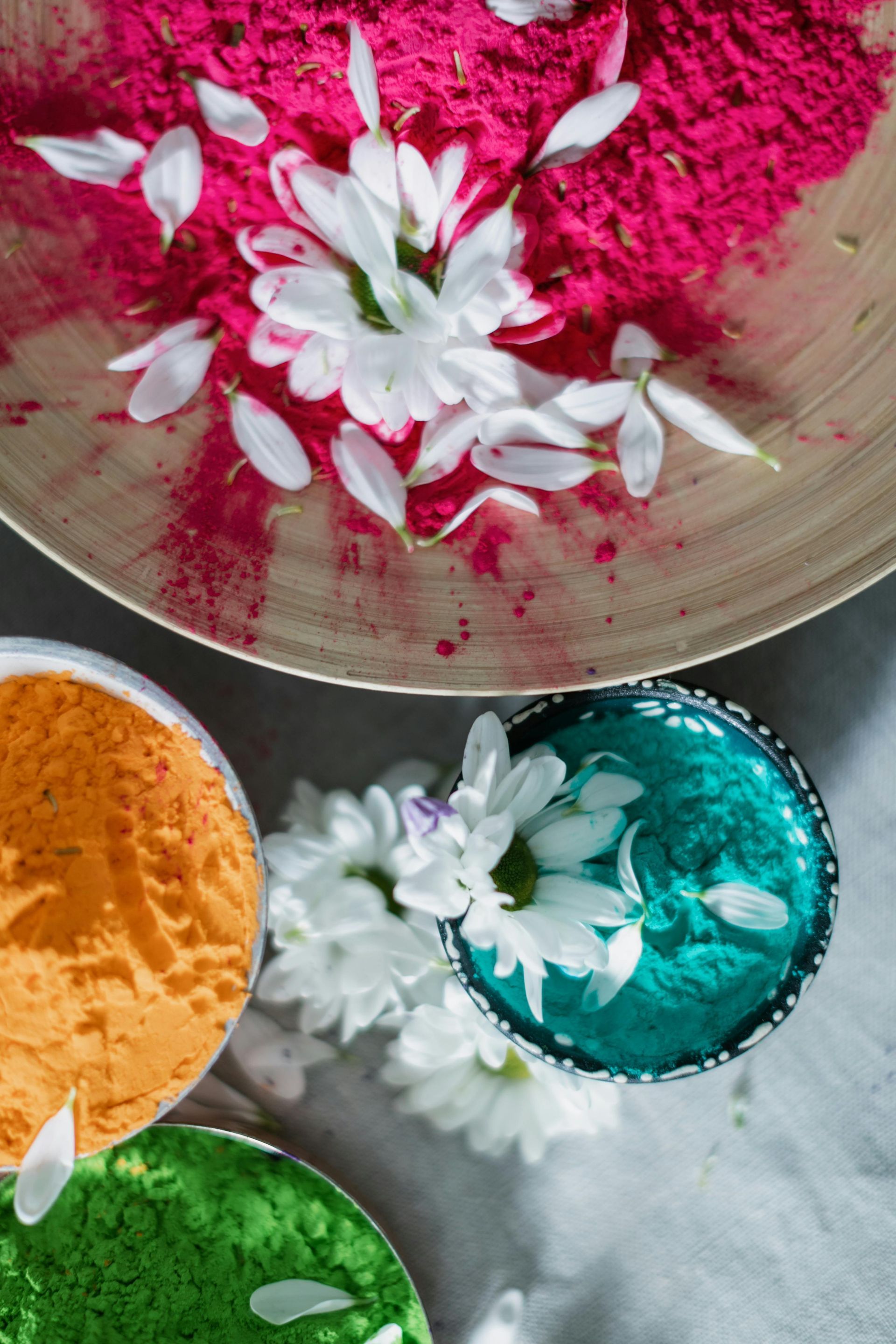 Ciotole di polvere rosa acceso, arancione, turchese e verde con fiori bianchi disposti sopra