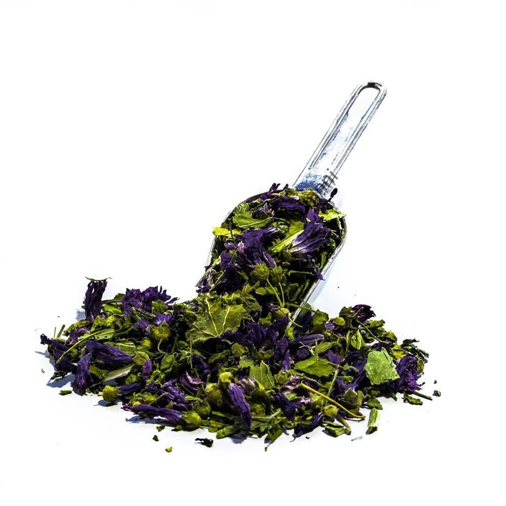 Un cucchiaio di vetro trasparente rovesciato su un mucchietto di foglie di tè sfuse viola e verdi.
