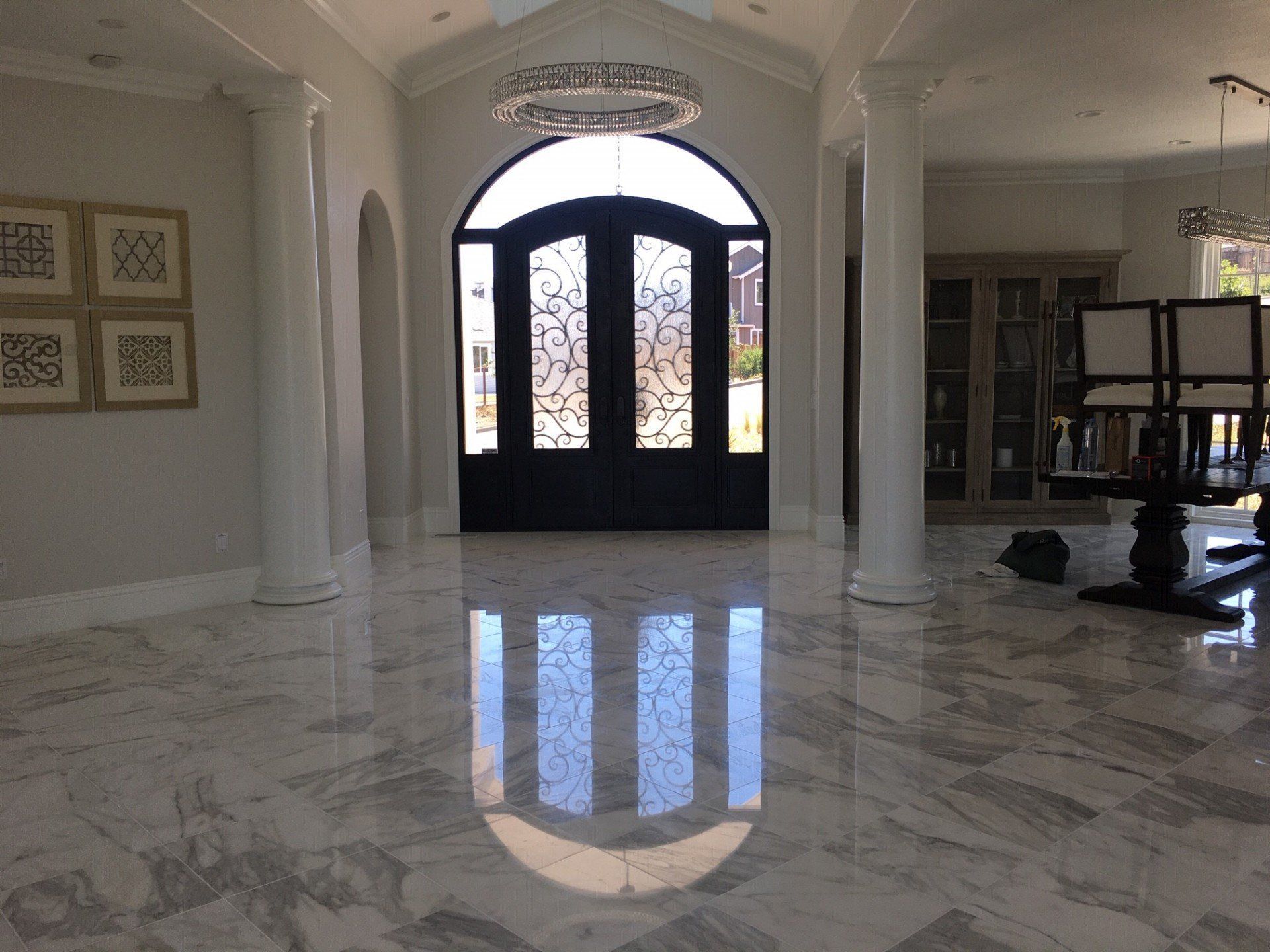Spacious, marble-floored entryway with arched black double doors, large columns, and a chandelier.