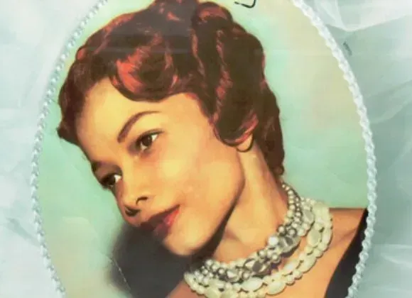 Vintage portrait of a woman with short auburn hair, wearing a pearl necklace against a pale green background