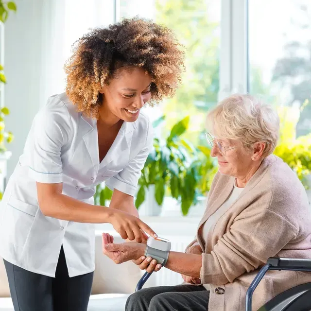 Caregiver checking blood pressure on an elderly woman in a bright home setting