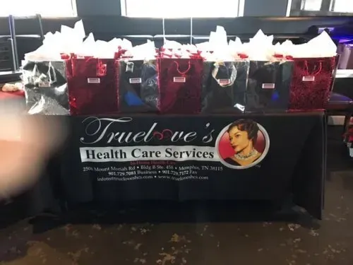Fundraising table with red gift bags and tissue paper for Truelove Health Care Services