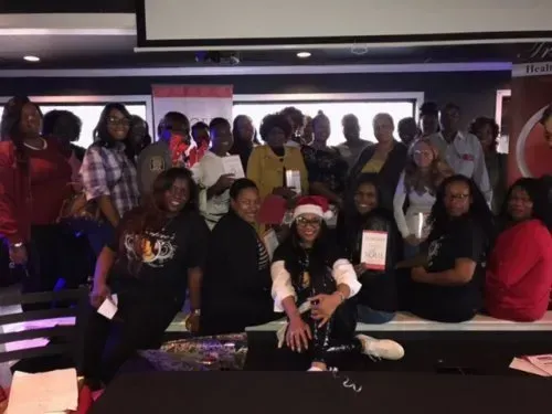Group of people posing indoors at a celebration, with one person in a Santa hat at the front.