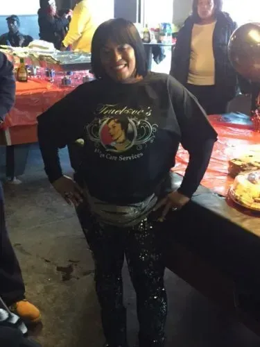 Woman posing at a brightly lit party table, wearing a black sweatshirt and sparkly pants.