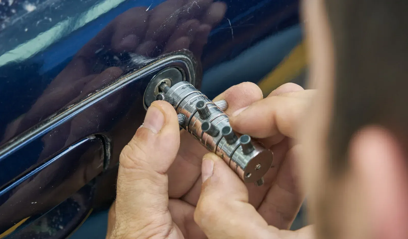 Person installing a silver lock mechanism into a blue car door.