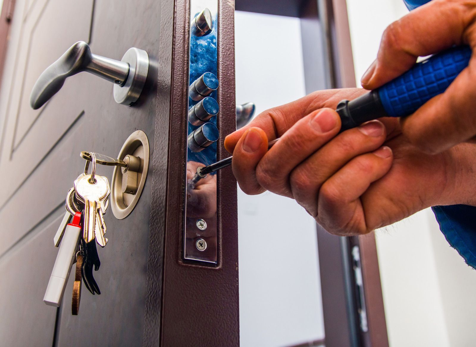 A person using a screwdriver on a door lock. A key ring hangs in the keyhole.